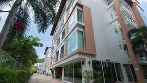 A modern building with a glass facade, a pool area, and a well-maintained garden with palm trees. - 639 2 Bedroom Contemporary Teak Wood Patong Beach (Patong)