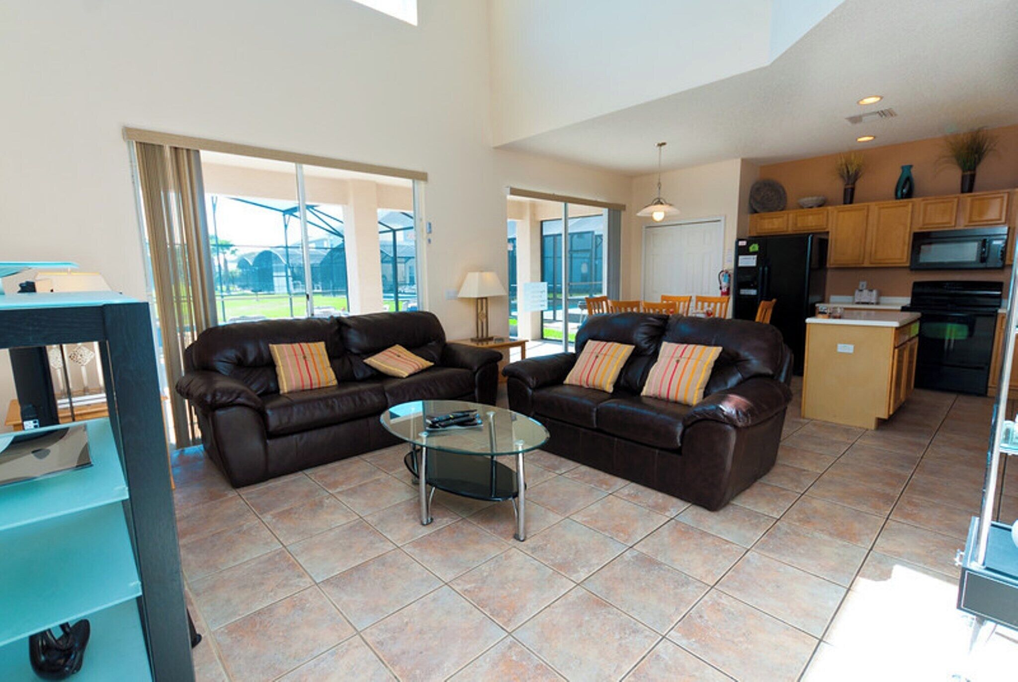 A spacious living area with two leather sofas, a glass coffee table, and a kitchen in the background.