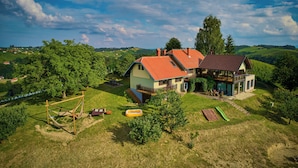 A house with a red roof, surrounded by a grassy yard with trees and a hammock. - Holiday House Podhamer Marijan (Ljutomer)