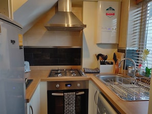 A compact kitchen with a gas stove, oven, and dishwasher, a sink with a dish rack, and a window with blinds.