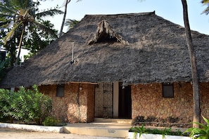 Una casa de techo de paja con fachada de piedra, entrada con reja y una ventana pequeña.