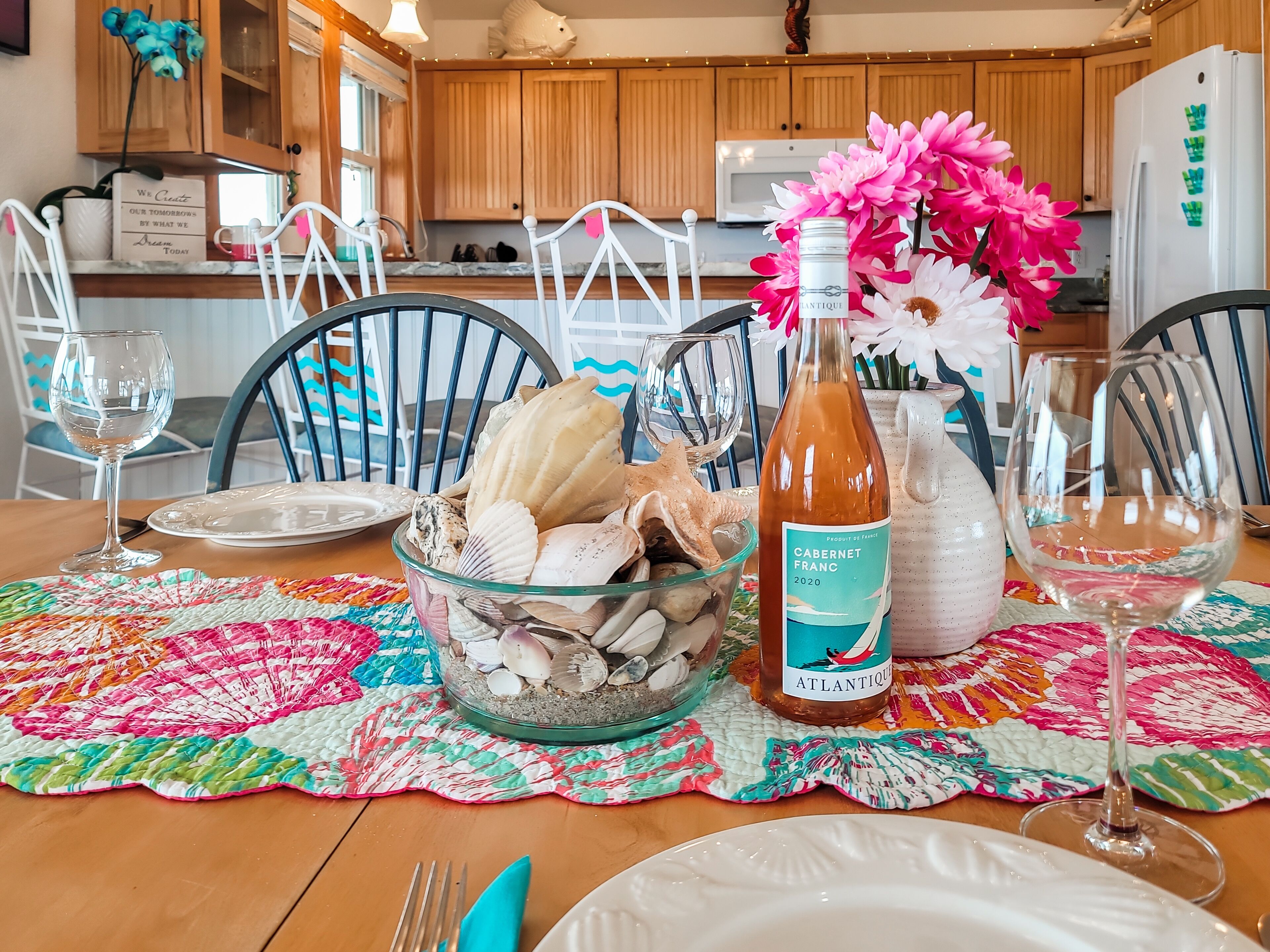 A dining table set with plates, a glass bowl of seashells, a bottle of wine, and a vase of flowers.