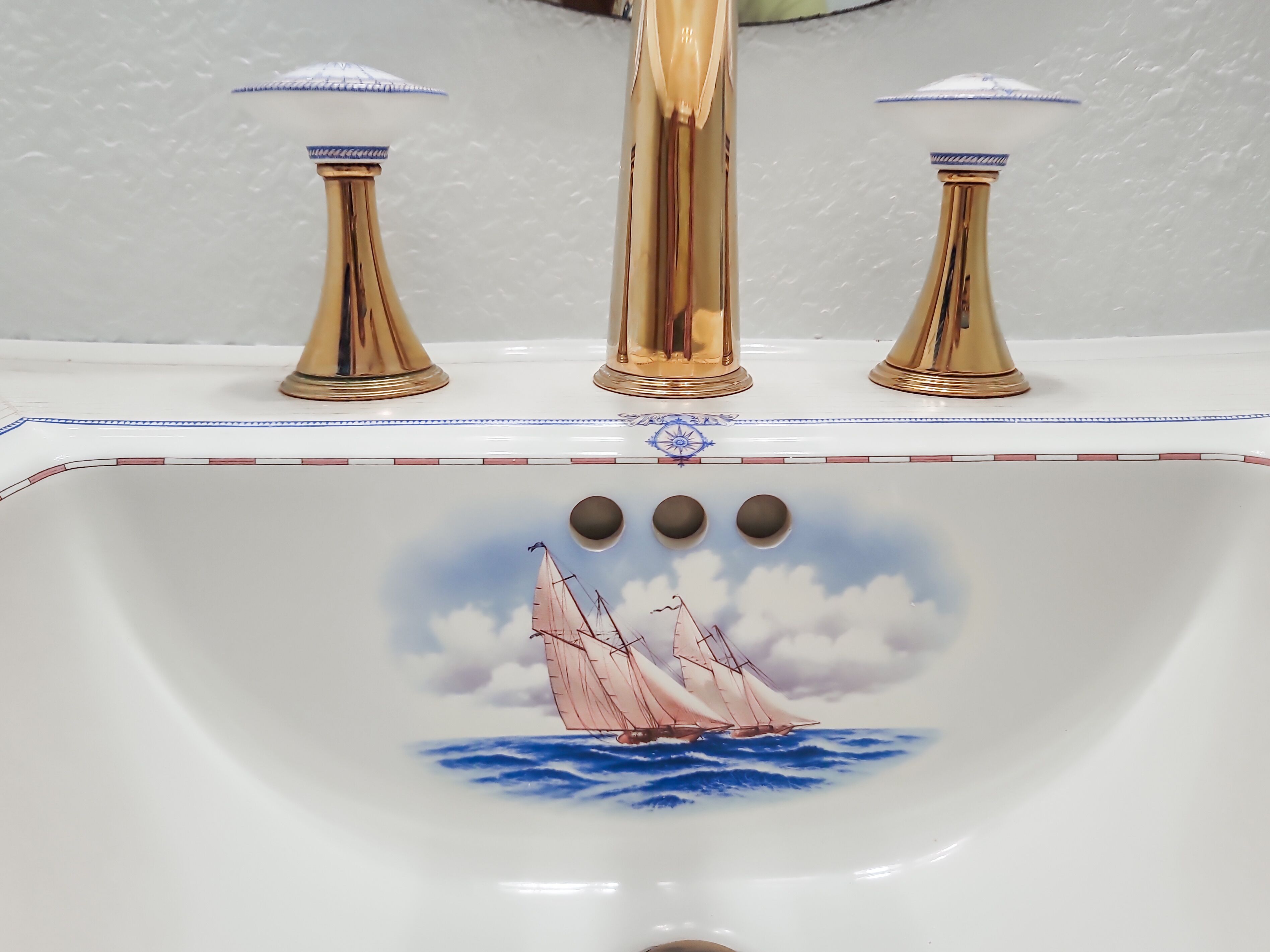A bathroom sink with a decorative design featuring a sailboat and a compass.