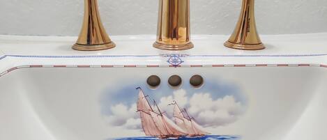 A bathroom sink with a decorative design featuring a sailboat and a compass.