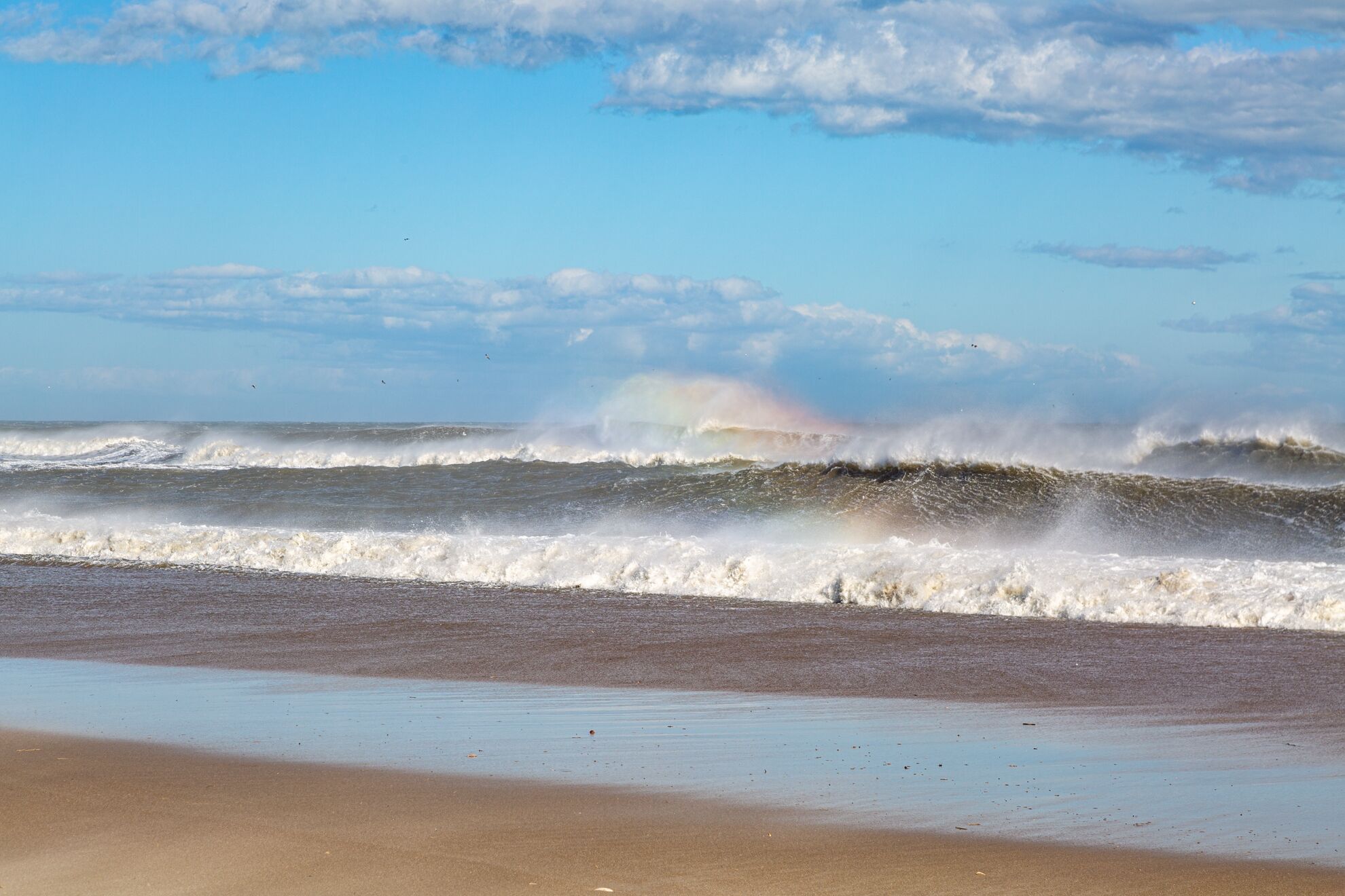 A beach with waves crashing onto the shore and a rainbow in the distance.