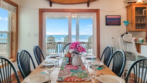 A dining area with a view of the ocean, a surfboard decoration, and a table set for a meal. - ON THE BEACH! Spiritual Sunrises and Glorious Sunsets, dogs welcome! (Rodanthe)
