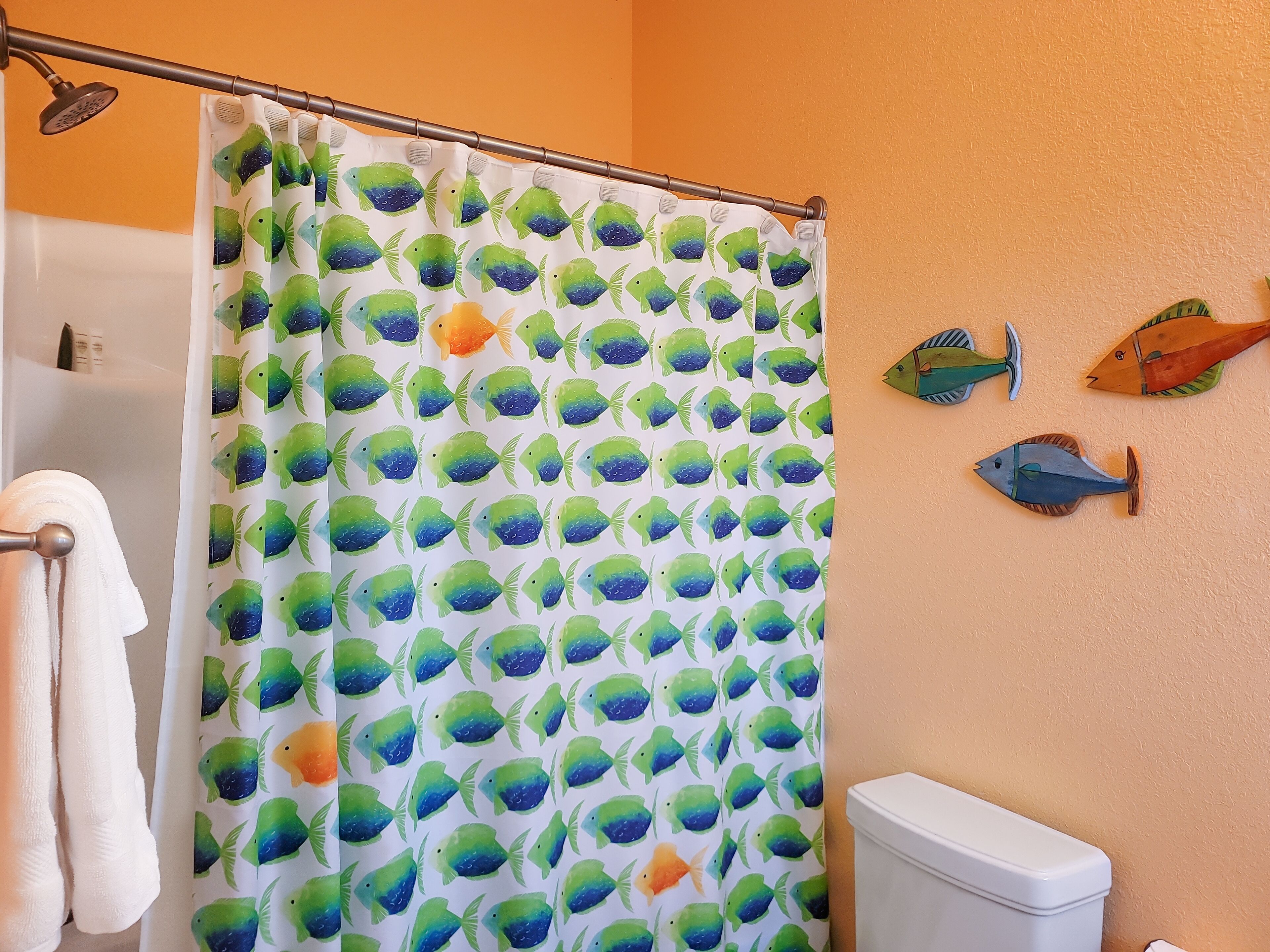 A bathroom with a shower curtain featuring a fish pattern, a toilet, and decorative fish wall art.