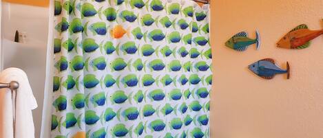 A bathroom with a shower curtain featuring a fish pattern, a toilet, and decorative fish wall art.