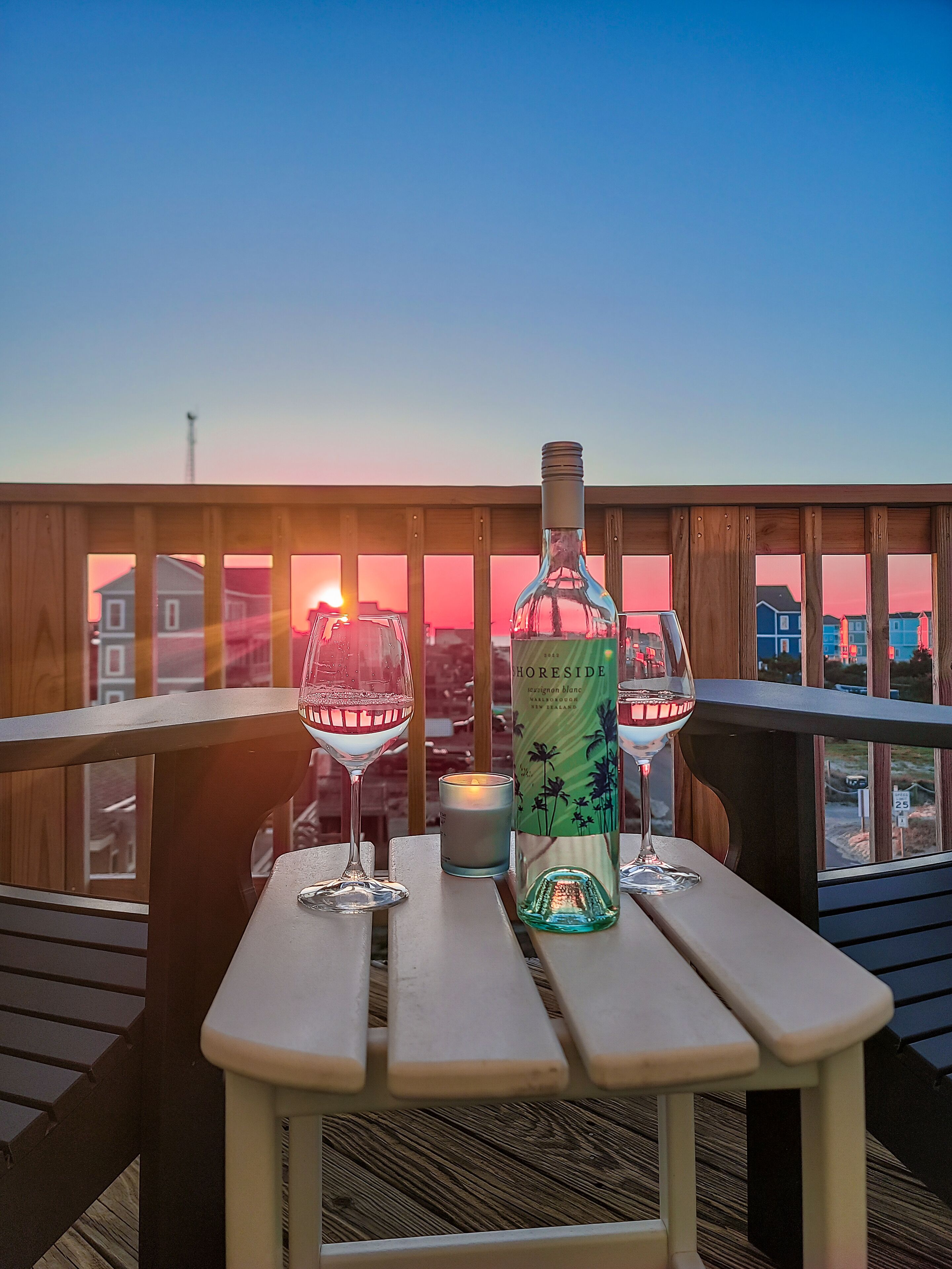 Een houten terras met een tafel voor twee personen, inclusief een fles wijn, glazen en een kaars.