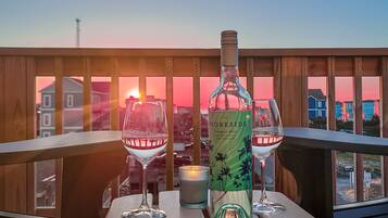 Een houten terras met een tafel voor twee personen, inclusief een fles wijn, glazen en een kaars.