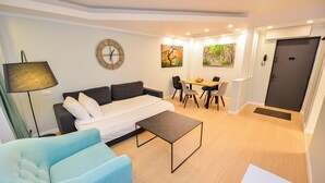 Un salon moderne comprenant un canapé, une table basse, une table à manger avec des chaises, une horloge et des œuvres d’art accrochées aux murs.