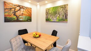 Un coin repas avec une table en bois, quatre chaises grises à revêtement rembourré et deux tableaux accrochés aux murs.