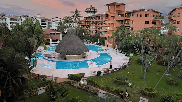 A resort with a central pool, palm trees, and a thatched-roof structure. - Sunny Apartment In The Heart of the Exclusive Marina Vallarta (Puerto Vallarta)