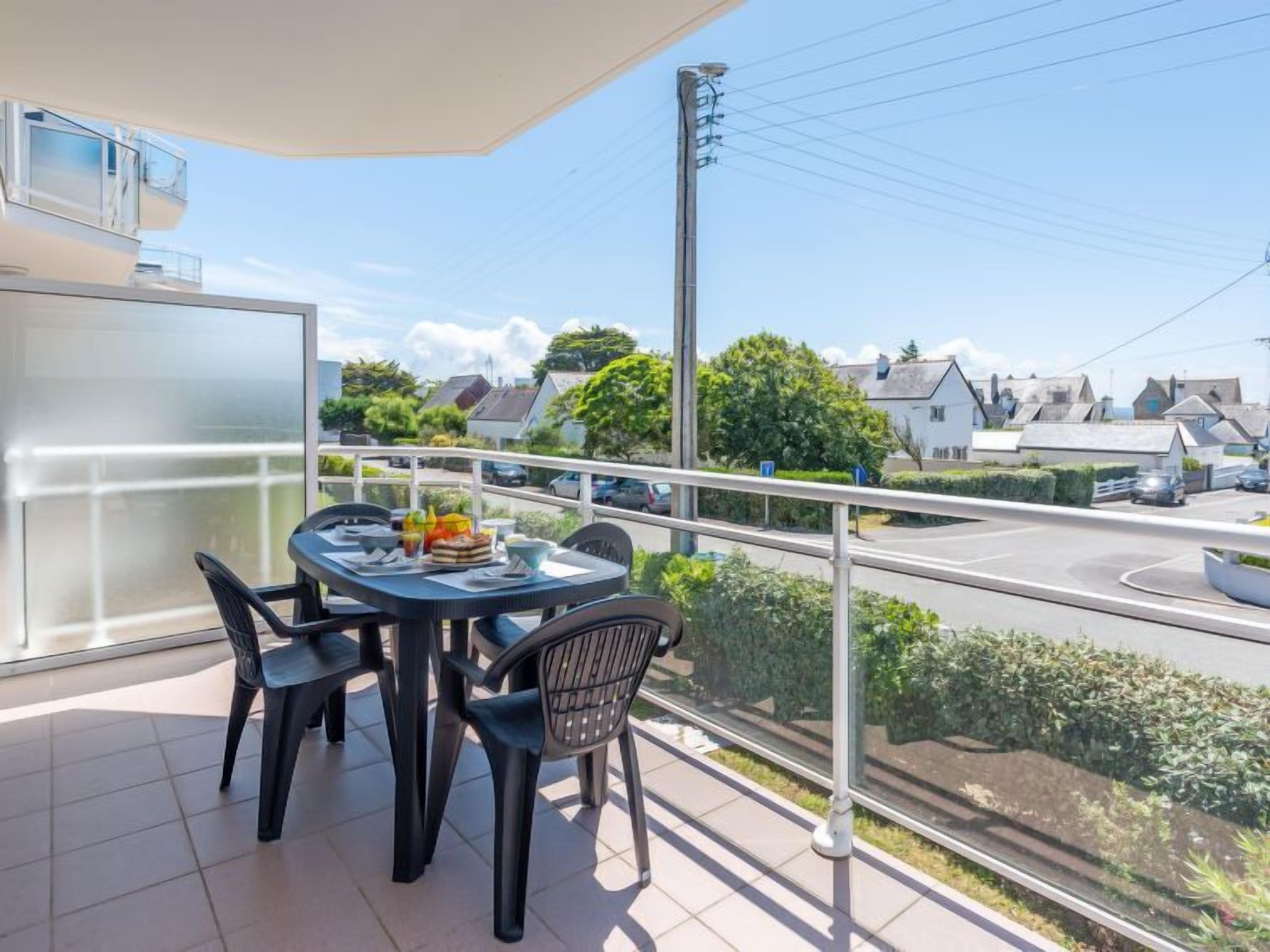 Een balkon met een tafel en stoelen, uitkijkend op een weg met huizen en auto's.