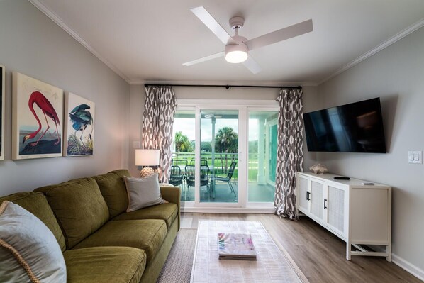 A living room with a sofa, a flat-screen TV, a ceiling fan, and a sliding glass door leading to an outdoor area.