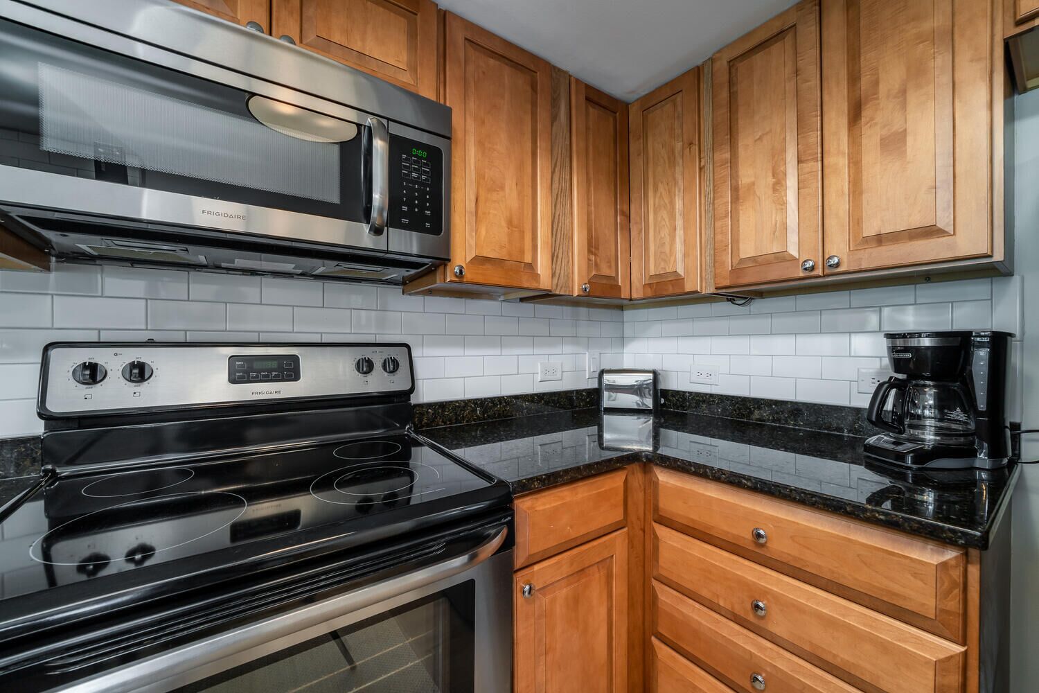Una cocina con microondas de acero inoxidable, estufa Frigidaire, armarios de madera, cafetera y tostadora.