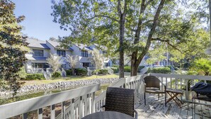 Une terrasse en bois avec des meubles en osier, un chemin de pierre et une vue sur des immeubles à plusieurs étages dotés de balcons.