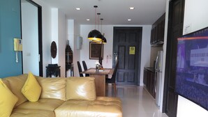 A modern living room with a leather sofa, a glass coffee table, and a dining area with a wooden table and chairs. - 6-38 - 2 Bdr Condo With Balcony and Shared Pool (Patong)