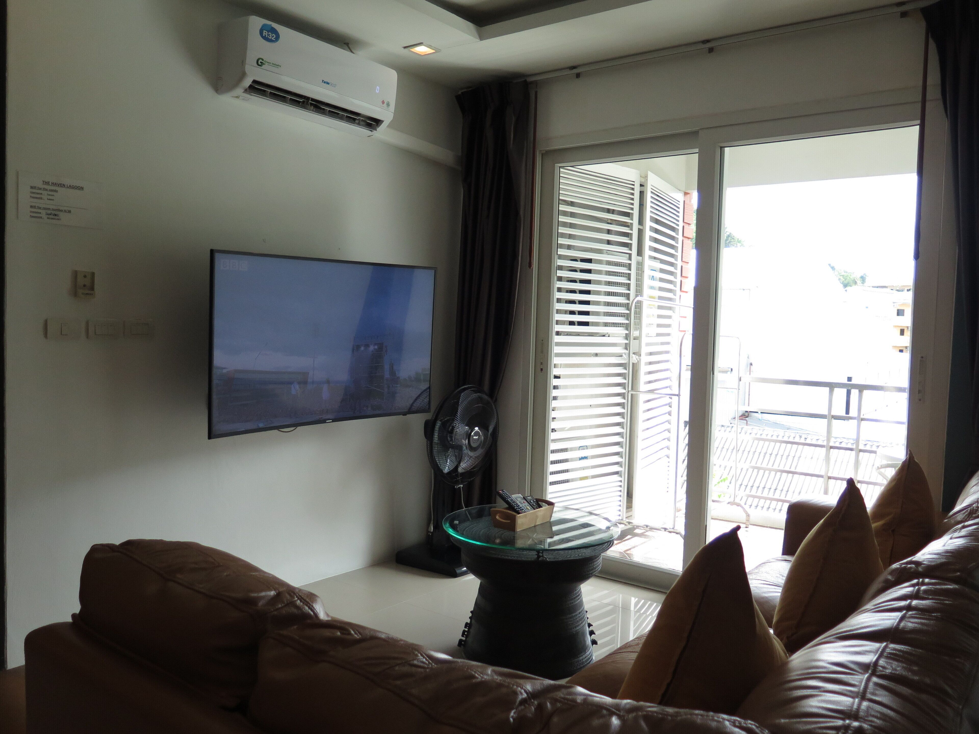 Un soggiorno con una TV a schermo piatto montata a parete, una ventola a soffitto e una porta vetrata scorrevole che dà su un balcone esterno.