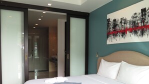 A hotel room with a bed, a painting on the wall, and a bathroom visible through an open door. - 6-38 - 2 Bdr Condo With Balcony and Shared Pool (Patong)