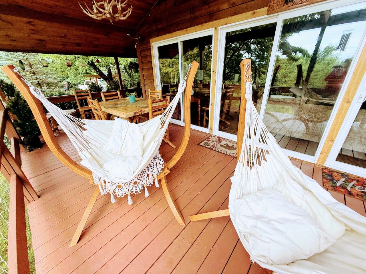 A wooden deck with two white hammocks and a table with chairs.