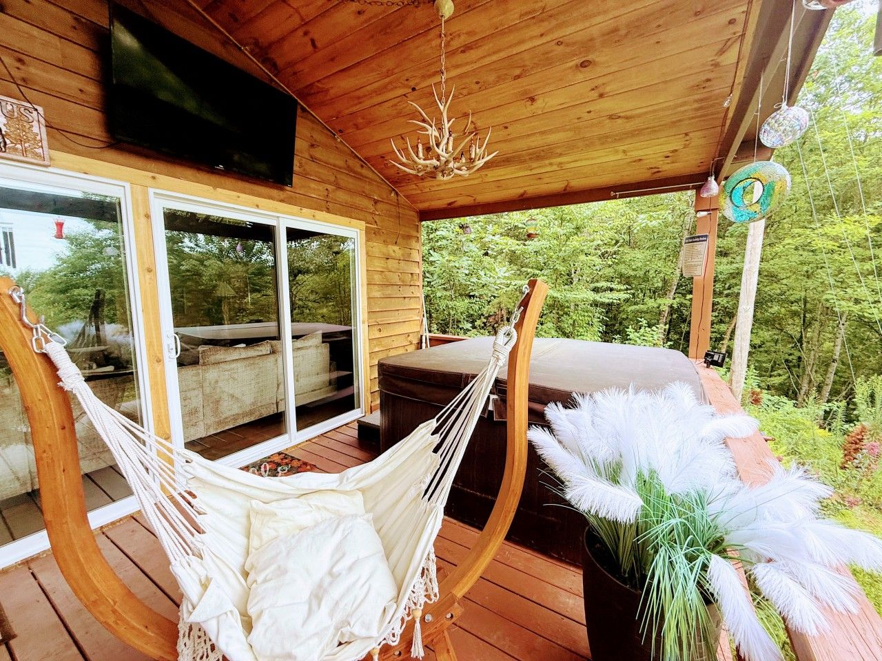A wooden deck with a hammock, a table with white feathers, and a television mounted on the wall.