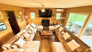 A log cabin interior with a large L-shaped sectional sofa, a fireplace, and a flat-screen TV mounted above it. - 4 Cabins/Mountain Views /Jacuzzi/Wi-Fi/Large Groups (Whittier)