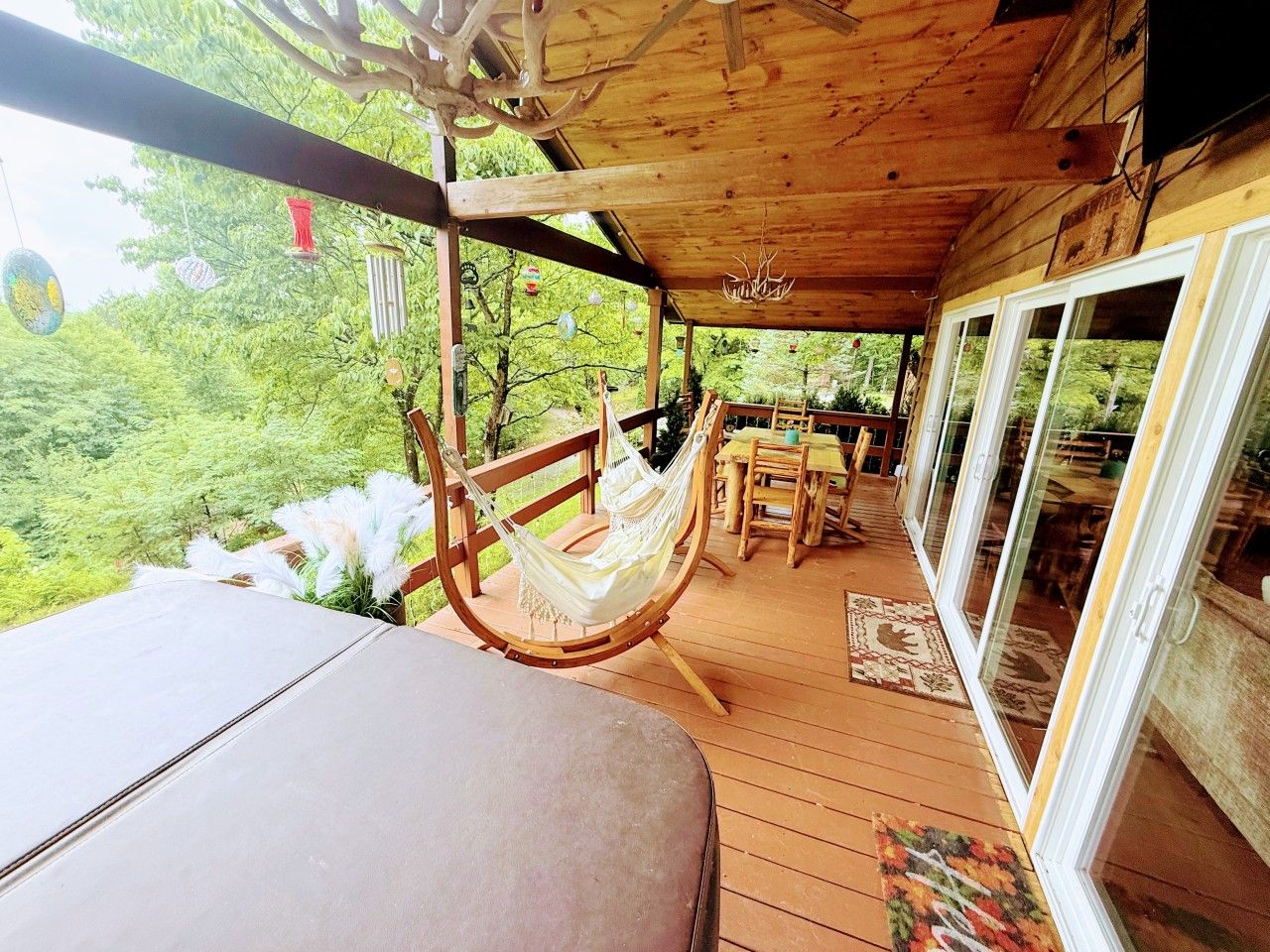 A wooden deck with a hammock, a table, and chairs, overlooking a lush green landscape.