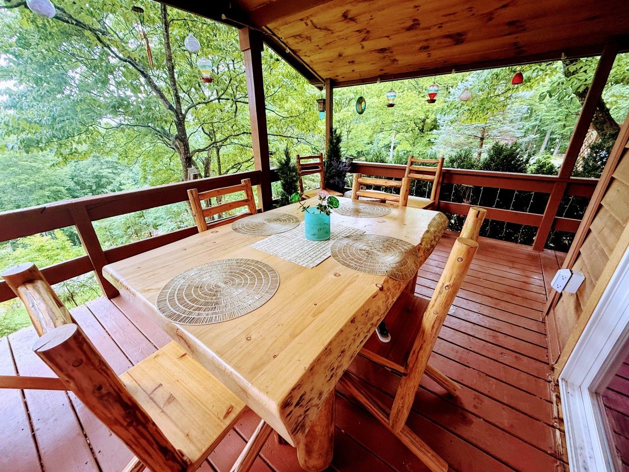 Een houten terras met een tafel en stoelen, omgeven door bomen.