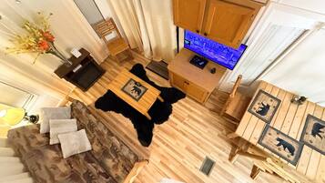 A room with a wooden floor, a black furry rug, a wooden table with a picture, a wooden cabinet, and a blue-lit kitchen area.