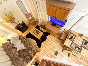 A room with a wooden floor, a black furry rug, a wooden table with a picture, a wooden cabinet, and a blue-lit kitchen area.