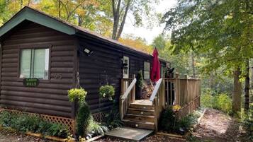 A cabin with a wooden exterior, a set of stairs leading to a deck, and a small garden area with plants and a hanging planter.