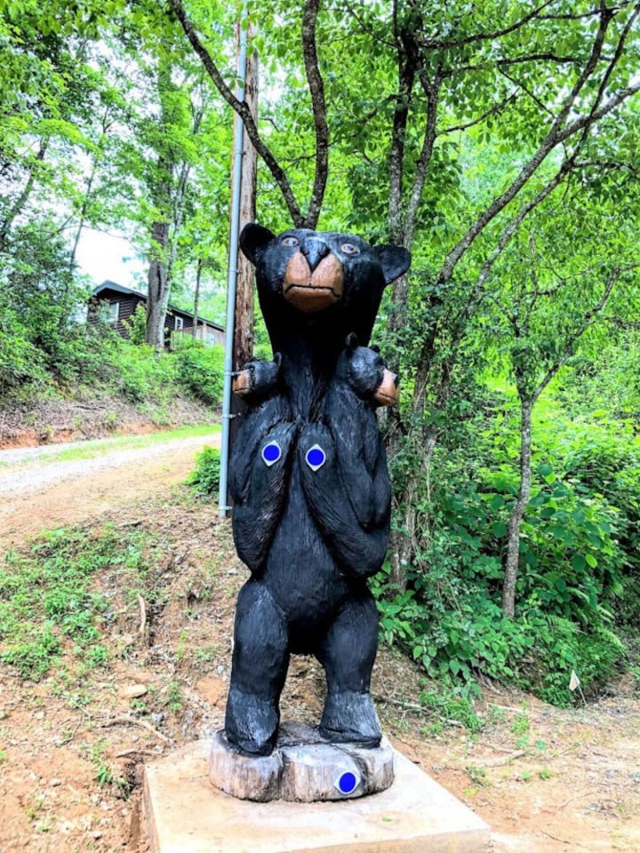 Una estatua de oso negro con ojos azules sobre una base de madera en un área boscosa.