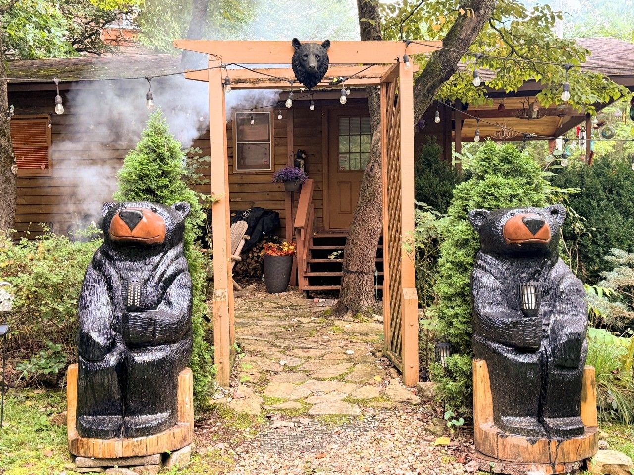 A wooden cabin with a bear statue at the entrance, a stone pathway, and a smoke-emitting chimney.