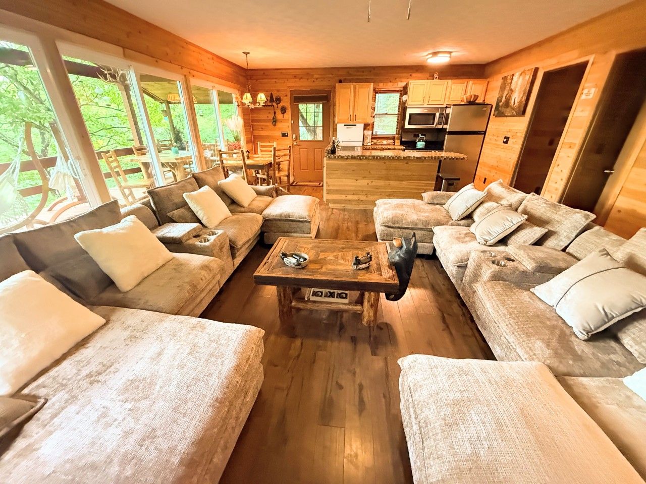 A cozy cabin interior with a central seating area, wooden furniture, and a kitchen in the background.
