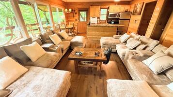 A cozy cabin interior with a central seating area, wooden furniture, and a kitchen in the background.