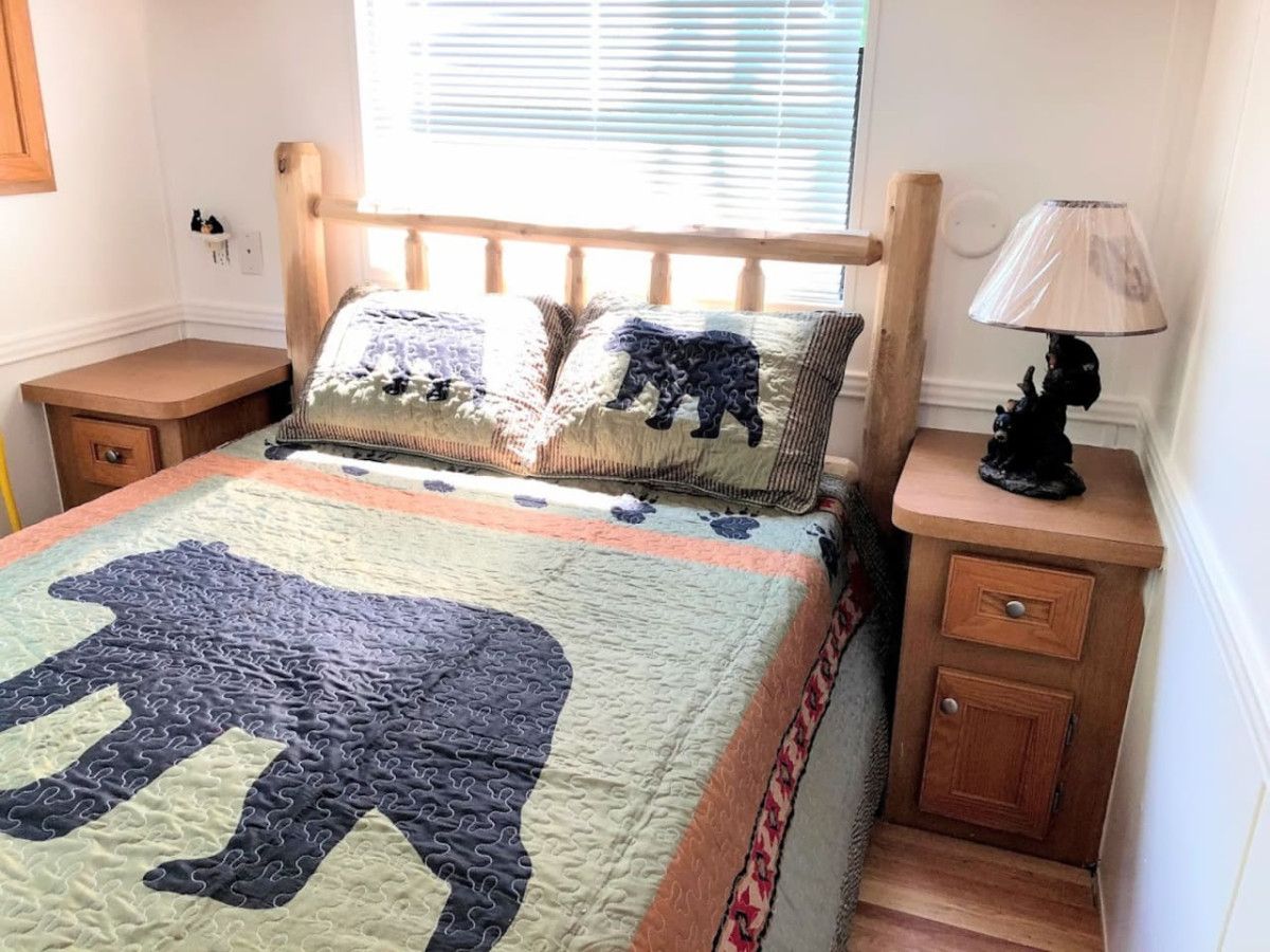 Un dormitorio con cama, mesita de noche, lámpara y ventana con persianas.