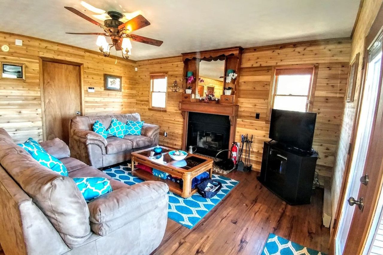A cozy cabin interior with a sofa set, a coffee table, a fireplace, and a television.
