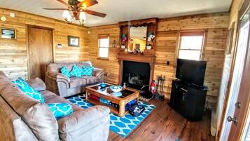 A cozy cabin interior with a sofa set, a coffee table, a fireplace, and a television.