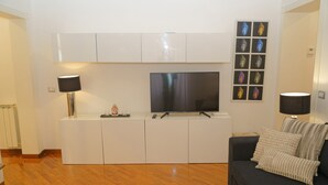 A modern living room with a flat-screen TV, white cabinets, a dark sofa, and a wall-mounted picture frame. - 2 Bedroom Trastevere (Rome)