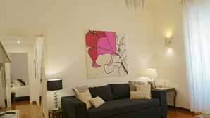 A living room with a dark-colored sofa, a small side table with a lamp, and a wall-mounted artwork. - 2 Bedroom Trastevere (Rome)