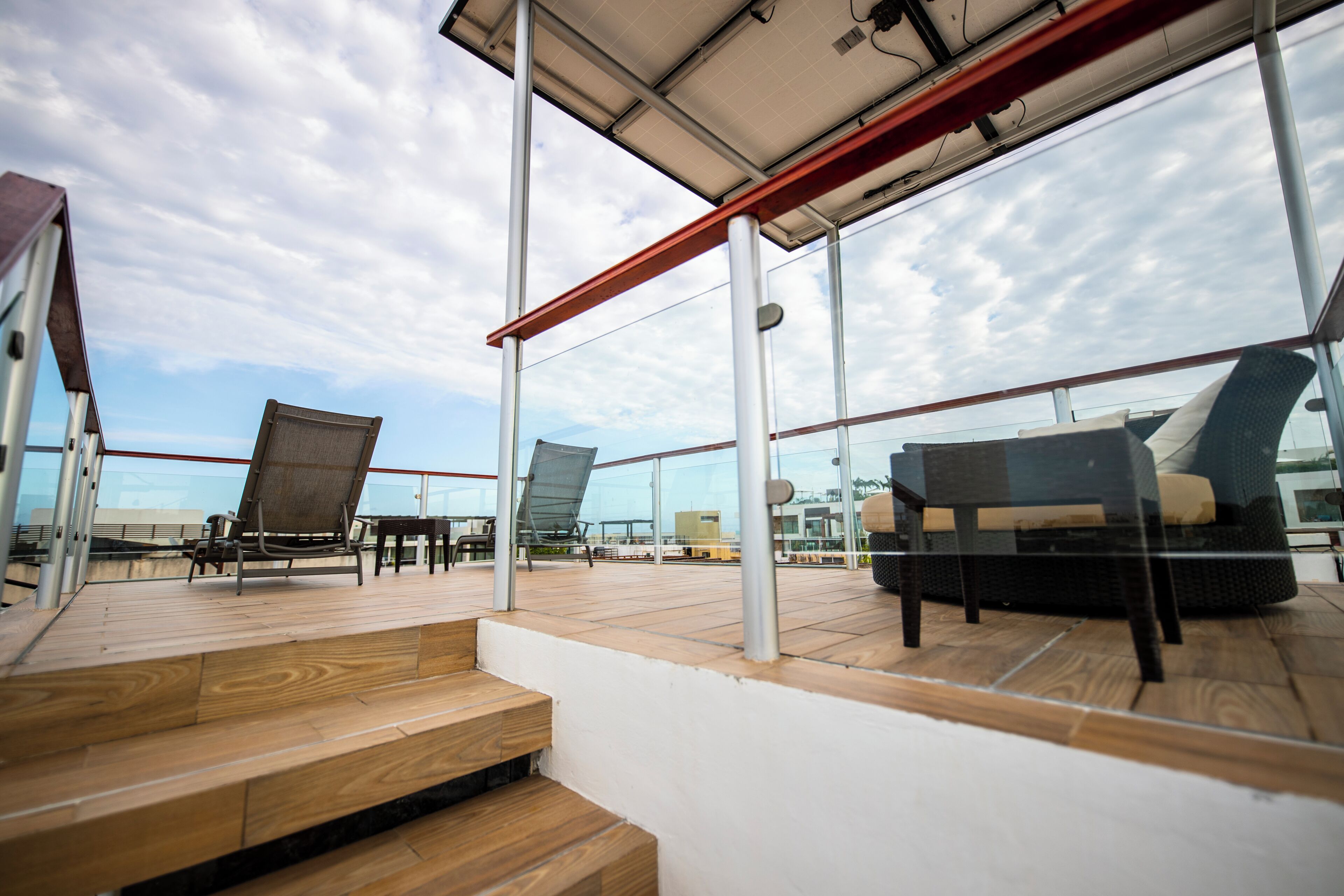Eine Dachterrasse mit Außenmöbeln, darunter eine Sitzecke mit Sofa und Stühlen, und eine Treppe nach oben.
