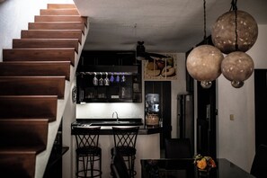 A kitchen with a wooden staircase, a bar area with stools, and a hanging light fixture.
