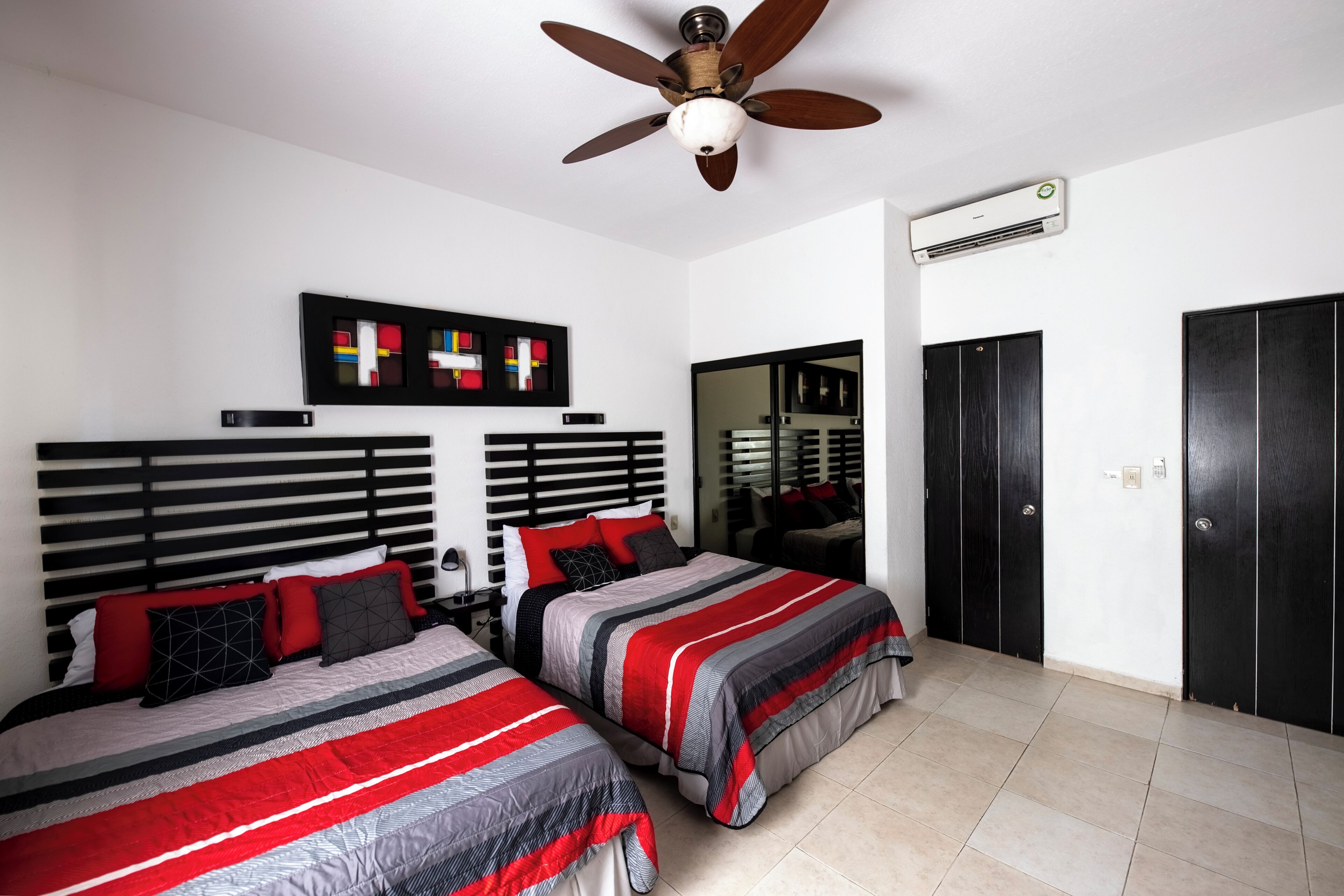 A bedroom with two beds, a ceiling fan, an air conditioning unit, and a wardrobe.