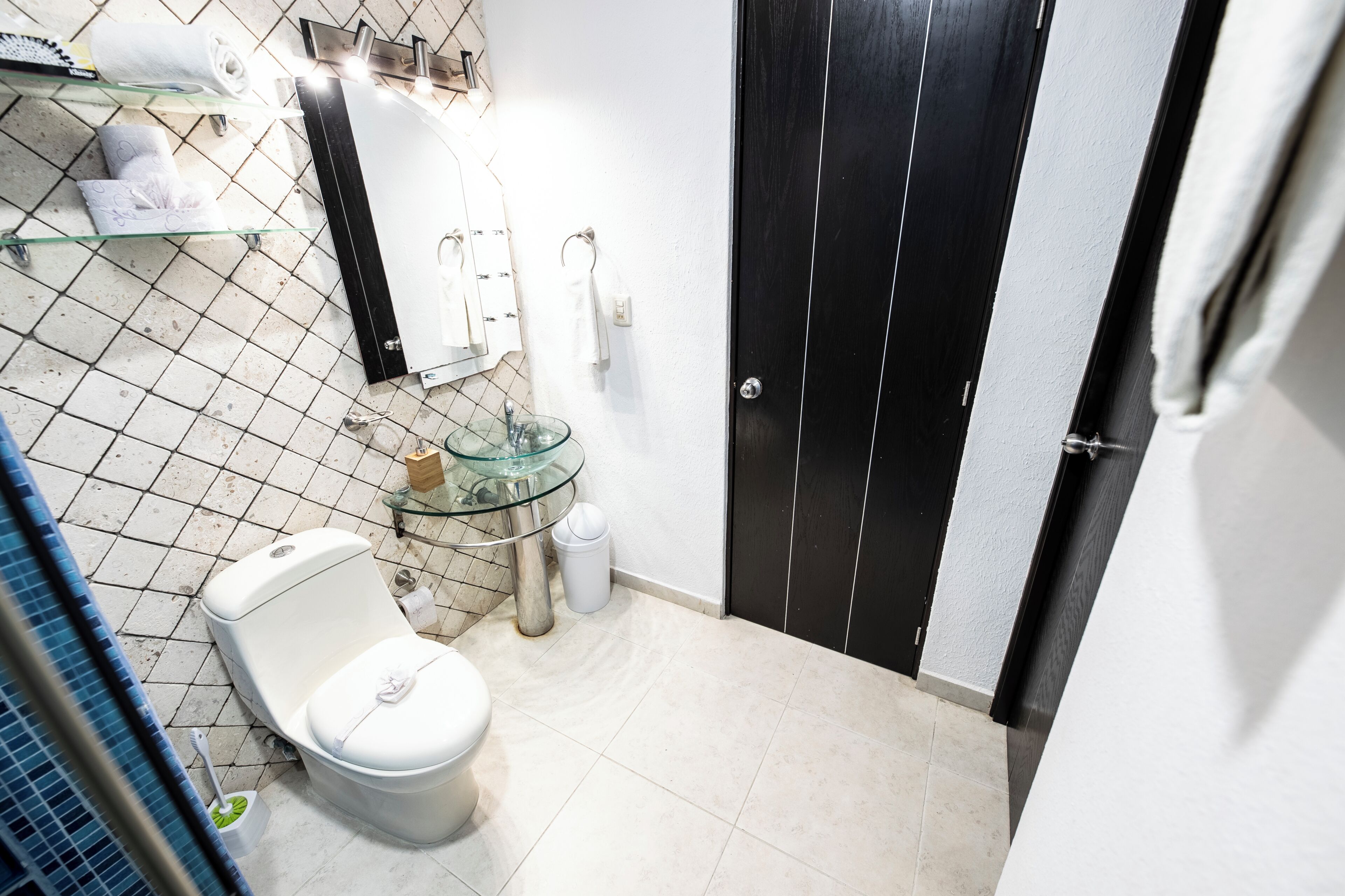 Une petite salle de bain avec des toilettes, un lavabo en verre et une porte noire.