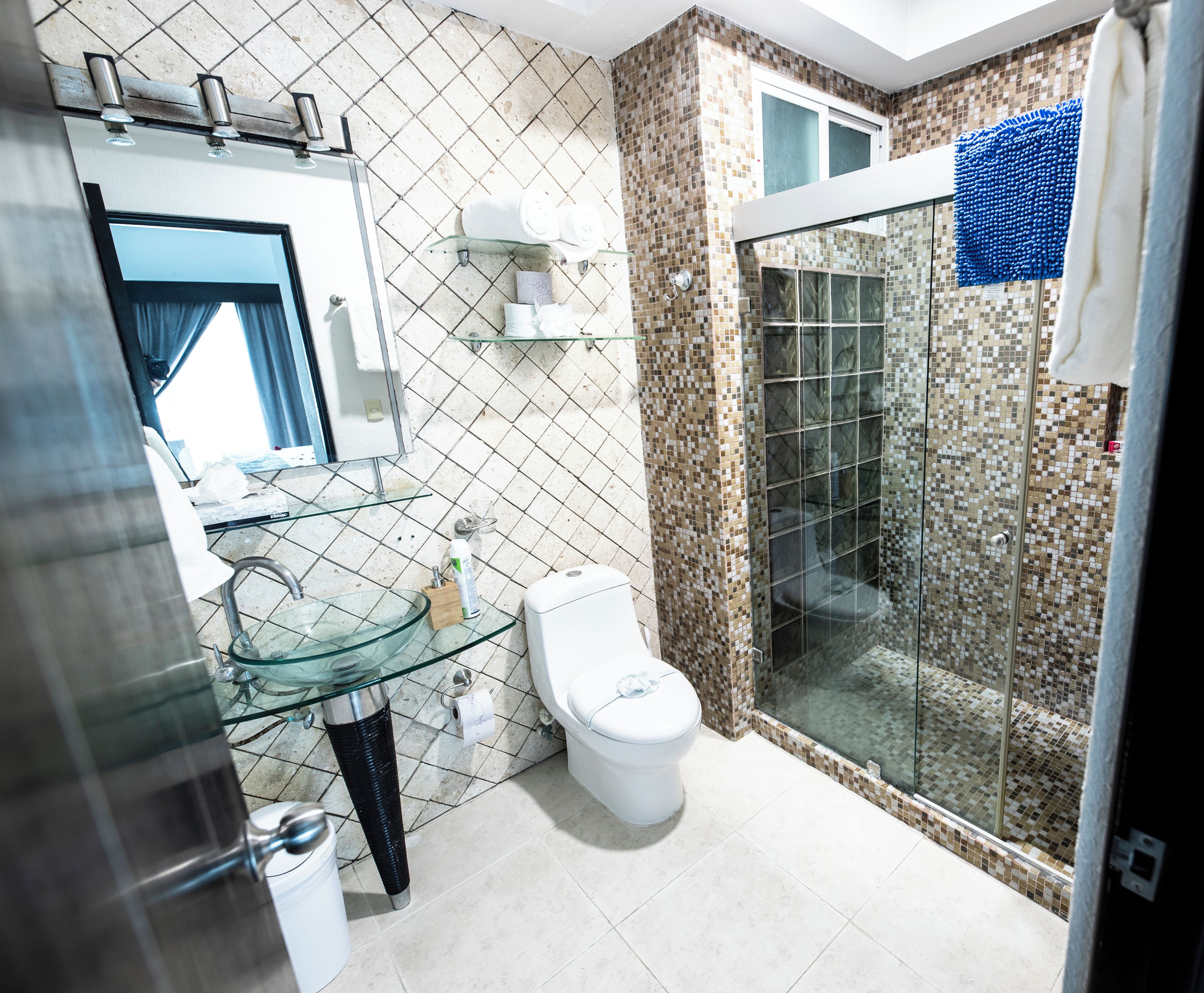 A bathroom with a glass shower enclosure, a toilet, and a glass sink.