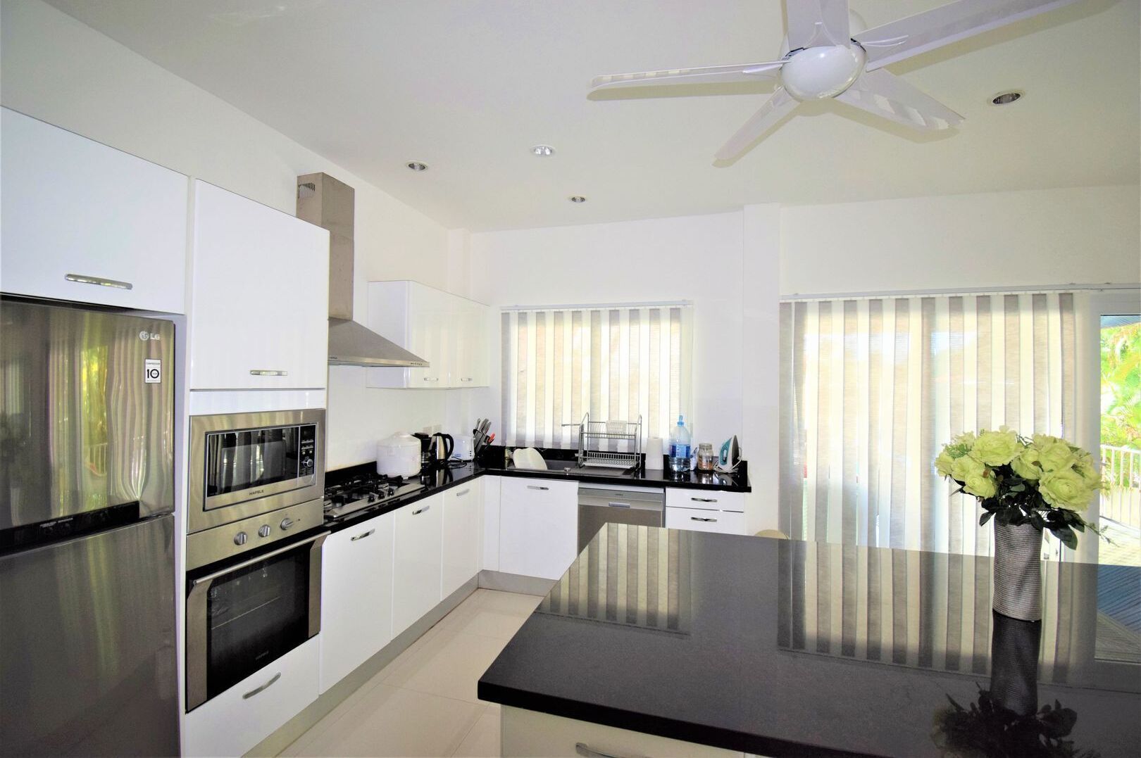 A modern kitchen with white cabinets, stainless steel appliances, a black countertop, and a ceiling fan.