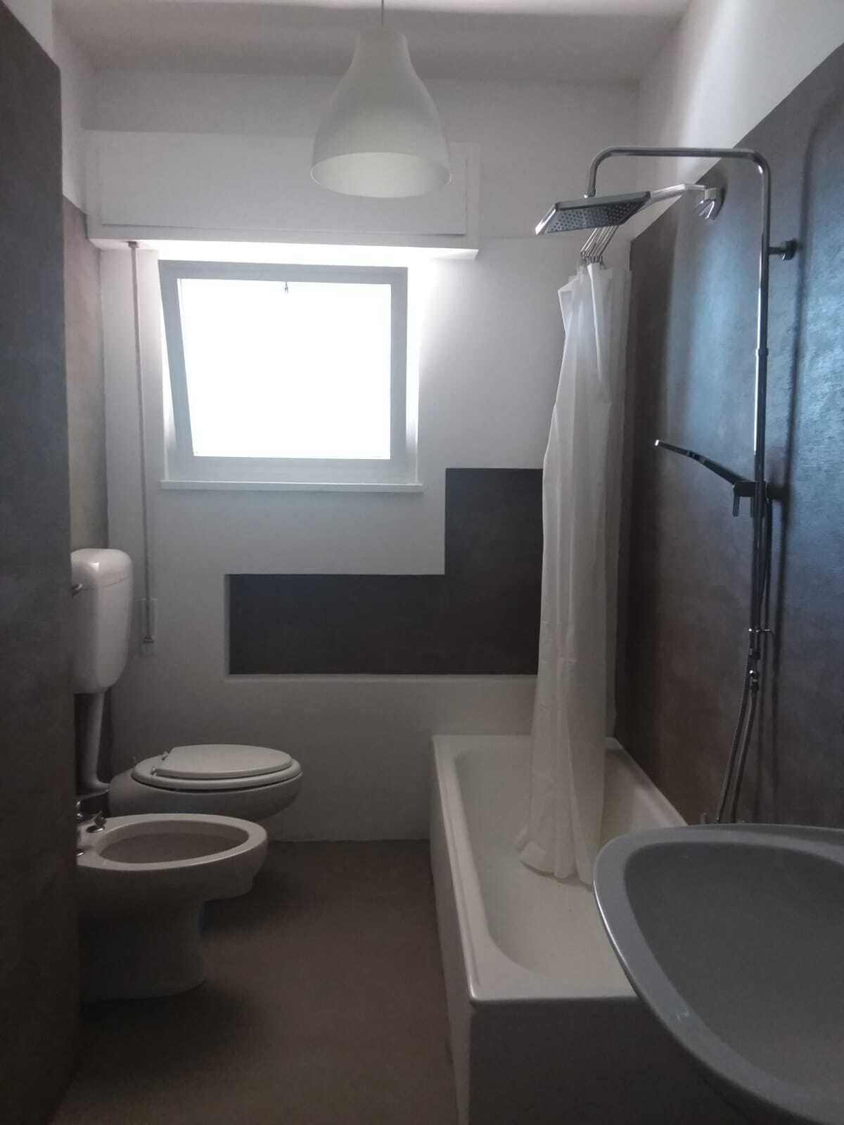 A compact bathroom with a toilet, bidet, and bathtub, featuring a window for natural light.