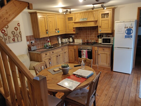 Une cuisine avec des meubles de rangement en bois, une table à manger avec des chaises, un réfrigérateur et un four à micro-ondes.