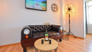 A living room with a leather sofa, a round table with a bottle of liquor, a television, a clock, and a floor lamp. - One by One - Adam's Studio - Cismigiu Gardens (Bucharest)